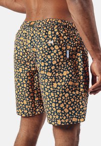 Patterned swim shorts in navy, featuring orange elephant designs. Elastic waistband, back pocket with snap closure, and smooth fabric texture.