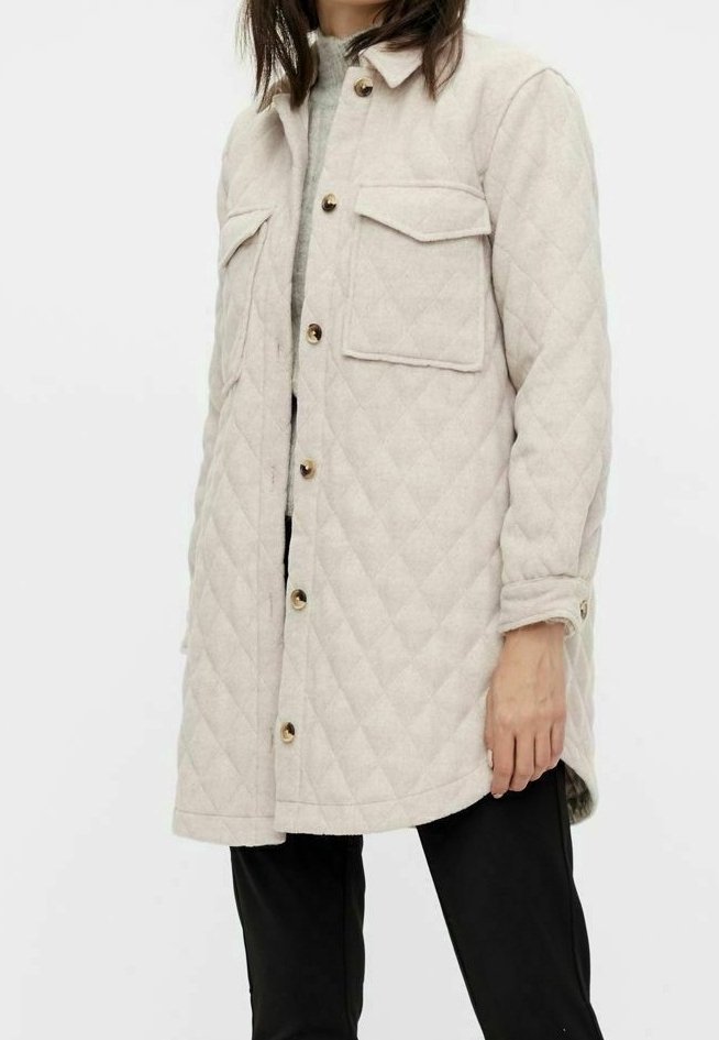 Abrigo acolchado beige con dos bolsillos en el pecho, botones dorados y un diseño de largo medio. Textura suave, mangas largas y ajuste casual.