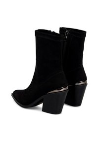 Botas de tobillo de ante negro con tacón cuadrado, cierre de cremallera en la parte trasera y acentos metálicos cerca del tacón. Textura suave y diseño ajustado.