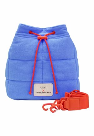 Sac seau matelassé bleu avec fermeture à cordon rouge et bandoulière rouge amovible, avec une étiquette blanche avec texte noir.