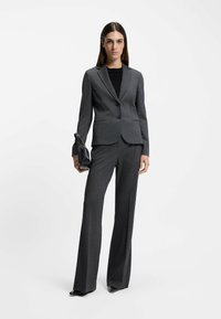 Completo a righe grigie che include un blazer aderente con due bottoni, pantaloni su misura e una clutch nera. Tacchi neri lucidi completano il look.