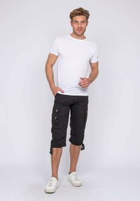 T-shirt blanc à manches courtes, pantalon cargo noir avec poches latérales et poignets à cordon, associé à des baskets blanches sur un fond uni.