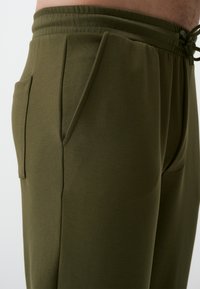 Olijfgroene joggingsbroek van zachte stof met een trekkoord in de taille, zijzakken en een taps toelopende pasvorm voor comfort.