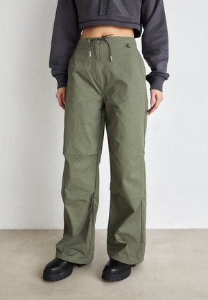 Olijfgroen wijde broek van een textiele stof met een trekkoord in de taille en accenten van zilverhardware. Gepaard met zwarte platformlaarzen.