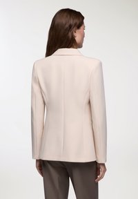 Blazer beige con vestibilità sartoriale, spalle strutturate e tessuto morbido. Caratterizzato da uno spacco posteriore singolo e senza hardware visibile.