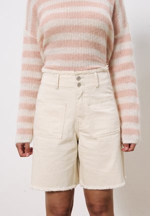 Beige denim short met een rafelige zoom, voorzien van twee voorkruiken en een dubbele knoopsluiting. Gepaard met een roze en witte gestreepte gebreide trui.