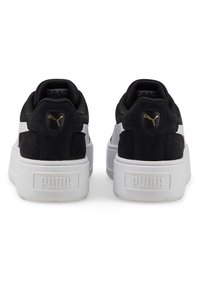 Zapatillas de ante negras con detalles en blanco y una gruesa suela blanca. Detalle del logo dorado en el talón. Forma redondeada y cuello acolchado.