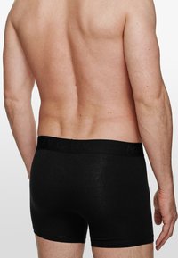 Schwarze Baumwoll-Boxershorts mit einem weichen, elastischen Bund, der dezente Markenkennzeichnung aufweist. Sanfte Textur und figurbetontes Design.