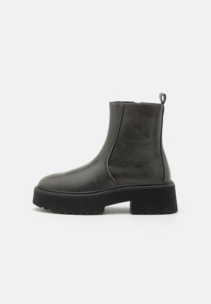 Bottines noires à tige synthétique lisse, avec des panneaux latéraux en élastique, une languette de tirage et une semelle en caoutchouc épaisse.