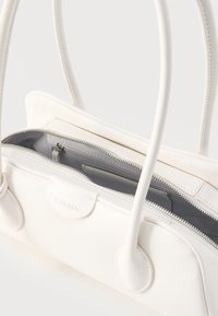 Λευκή τσάντα χειρός Calvin Klein με διπλές στρογγυλές λαβές, μερικώς ανοιχτό φερμουάρ στην κορυφή και ορατή εσωτερική τσέπη και επένδυση.