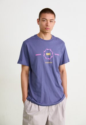 Lilla bomull T-skjorte med et sentralt grafisk trykk av "NIKE" i gult og rosa aksenter. Korte ermer og rund hals design.