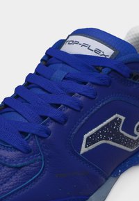 Niebieski but sportowy z teksturowanymi sznurowadłami, białym i srebrnym logo po boku oraz etykietą „TOP-FLEX” na języku.