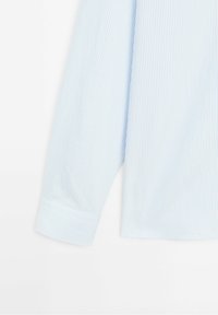 Manche longue d'une chemise à fines rayures bleu clair et blanc avec un poignet boutonné sur un fond blanc.