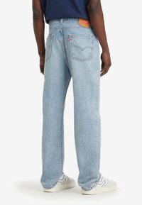 Jean en denim bleu clair avec une coupe ample, cinq poches et un patch en cuir de la marque sur la taille arrière. Portés avec des baskets blanches.