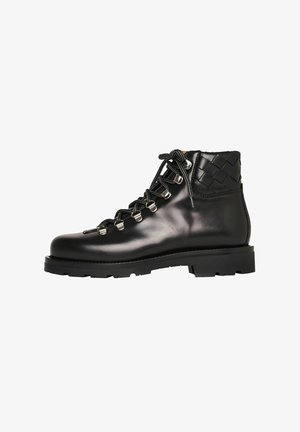 Schwarze Leder-Ankle Boots mit dicker Sohle, metallischen Ösen, schwarzen Schnürsenkeln und geflochtenen Lederdetails an der gepolsterten Knöchelpartie, Seitenansicht.