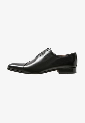 Chaussure habillée en cuir noir avec une finition lisse, bout rond, six œillets pour les lacets et un talon bas empilé. Design minimaliste.