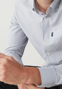 Chemise à manches longues en blanc et bleu rayé, en coton, col boutonné, poche poitrine unique, détail de logo subtil sur la poche.