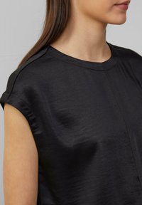 Haut noir à manches courtes avec une texture lisse et légèrement brillante, présentant un col rond et des détails de couture subtils.