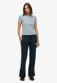 Striped blue and white cotton t-shirt paired with navy sweatpants featuring side stripes and logo, worn with dark shoes.