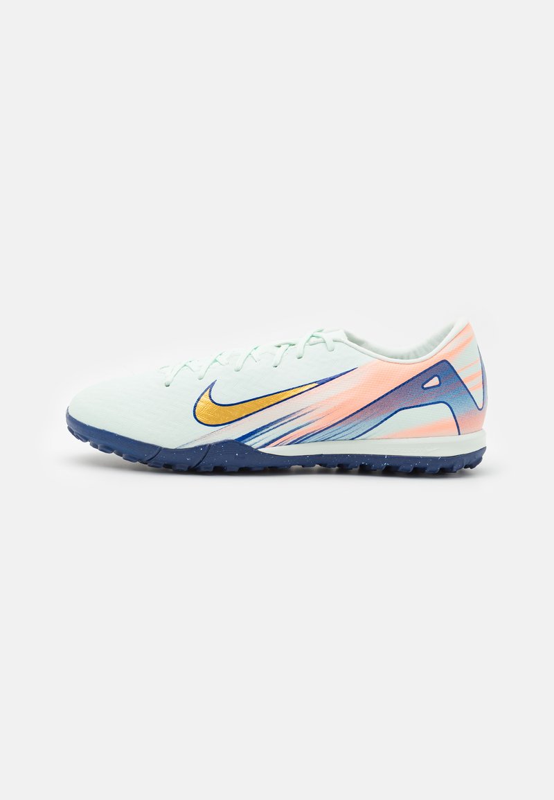 White and peach Nike turf soccer shoe with dark blue sole and gold swoosh, side view on a plain light background.