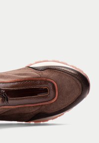 Sneaker in suede marrone con un accento in pelle liscia, dotato di una suola in gomma rosa e una punta arrotondata. Dettaglio con zip su un lato.