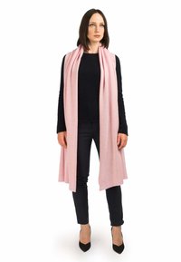 Pink cashmere tørklæde draperet over en sort sweater, der står i kontrast til mørke bukser og sorte hæle, hvilket skaber et blødt, lagdelt look.
