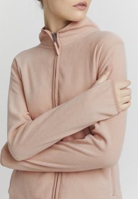 Lichtroze fleece jas met een hoge kraag en een volledige rits aan de voorkant. Heeft lange mouwen met strakke manchetten en een zachte, gestructureerde stof.