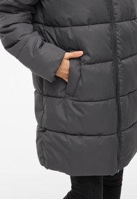 Šedá prešívaná bunda s predným zipsom, horizontálnym prešívaním a bočnými vreckami. Materiál pôsobí mäkko a je izolovaný pre teplo.