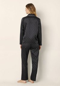 Zwart satijnen pyjama set met lange mouwen en broek, gekenmerkt door een verticale wit en rood gestreepte print, een gladde textuur en een klassieke kraag.