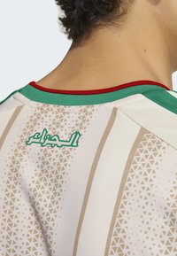 Wit shirt met groene, rode en gouden accenten; voorzien van een geometrisch patroon en Arabische tekst op de achterkant. Zacht, lichtgewicht materiaal.