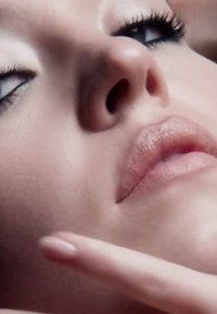 Nahaufnahme eines Gesichts mit glatter, heller Haut, hellroten Lippen und definierter Augen-Make-up, einschließlich dunklem Eyeliner und langen Wimpern.