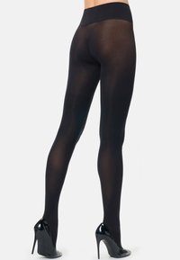 Collant neri opachi con vita alta, texture liscia e finitura lucida, indossati con scarpe con tacco alto nere, che mettono in mostra le gambe da dietro.