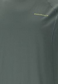 Tummanvihreä liikuntapaita, joka on valmistettu kosteusasioita siirtävästä kankaasta. Paidassa on teksturoitu pinta ja "ENDURANCE"-logo keltaisena.