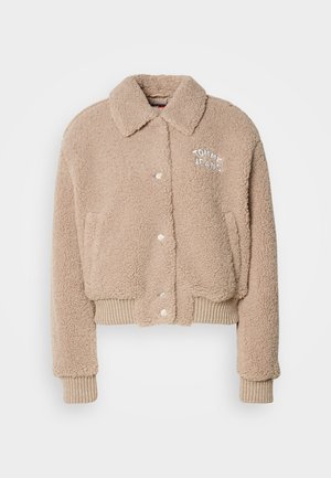 Beige plysjakke med cropped længde, knaplukning, ribstrik nederst og ved ærmerne, samt broderet "TOMMY JEANS" logo på venstre bryst.