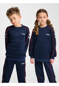 Marinnsportset bestående av långärmade tröjor och byxor med röda accenter och vitt logotyp. Mjuk, slät tyg med randiga detaljer på ärmarna.