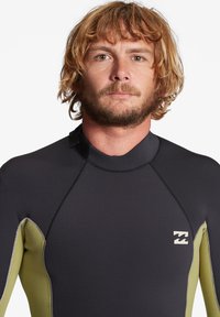 Black and olive green wetsuit with a textured finish, featuring a tight fit, smooth seams, and a logo on the chest. No zippers visible.
