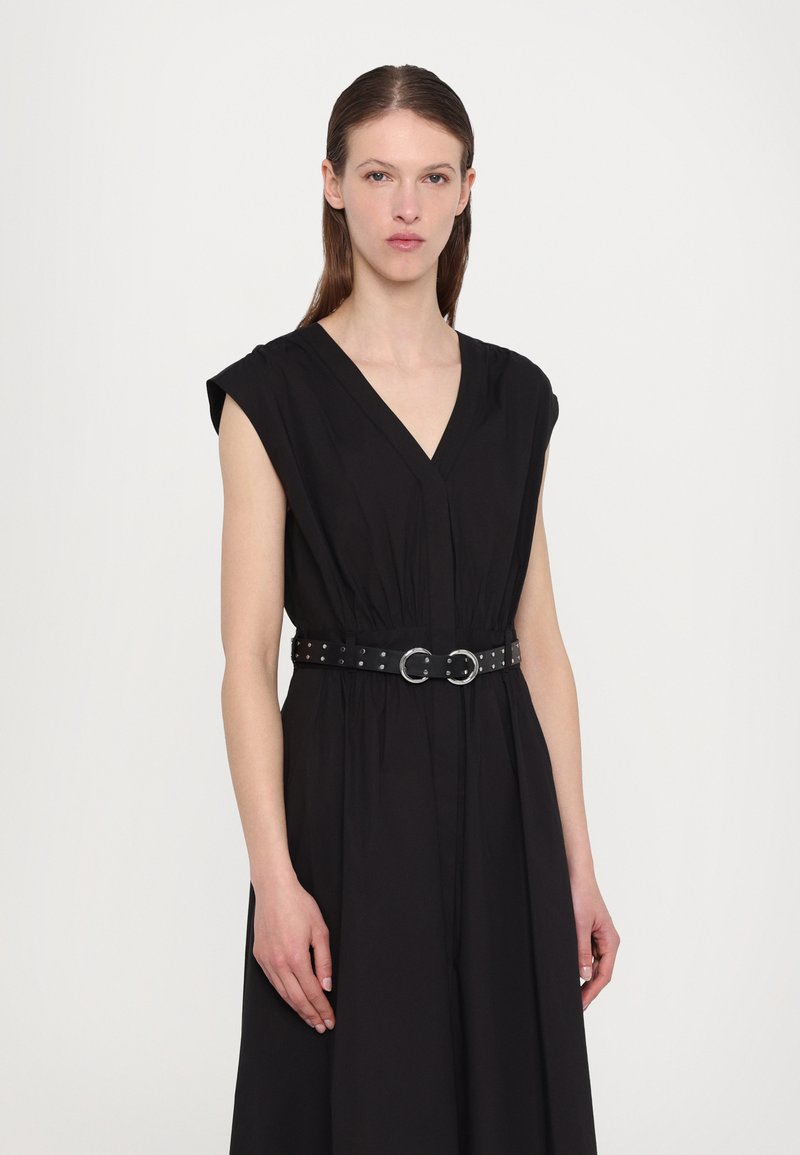 Vestido negro con un escote en V profundo y mangas cortas, ajustado a la cintura con un cinturón negro adornado con tachuelas y con detalles de hardware en plata.
