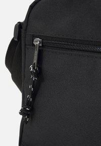 Bolsa de tela negra con textura suave, que cuenta con un cierre de metal y un cordón de tiro anudado en blanco y negro.