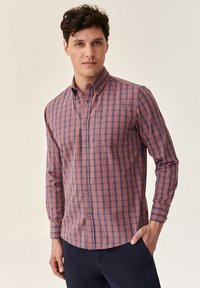 Long-sleeve button-up shirt in red and navy plaid pattern with a pointed collar and chest pocket, made of lightweight fabric.
