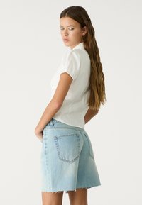 Bela bluzica s puf rukavima in ovratnikom, združena s svetlo modrimi denim kratkimi hlačami s frufru robom in dvema zadnjima žepoma.