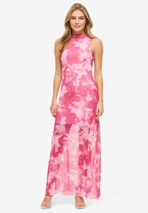 Femme portant une robe maxi sans manches à motifs rose et blanc avec un col haut et un panneau inférieur transparent, debout les bras le long du corps.