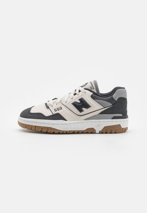 Nízké tenisky New Balance 550 v béžové, černé a šedé barvě s bílou mezipodešví a podešví z gumy, boční pohled.
