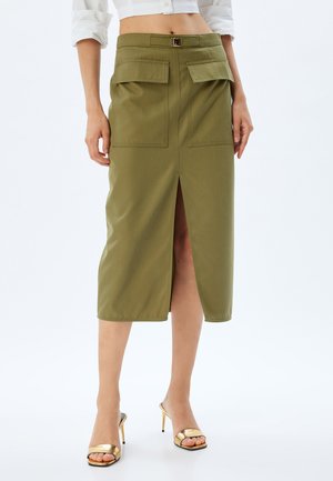 Jupe midi en coton vert olive avec une fente avant, deux poches supérieures et un détail de ceinture à la taille. Texture lisse, design classique.
