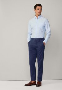 Camicia a righe blu chiaro con bottoni abbinata a pantaloni chino blu navy e mocassini marroni. La camicia ha una tasca sul petto e maniche lunghe.