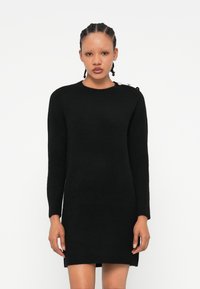 Vestido preto de malha com mangas longas, decote redondo e pormenores canelados na bainha. Apresenta botões decorativos no ombro.