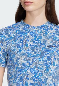 Short-sleeve, round-neck shirt featuring a blue floral pattern on a light blue background; includes black Adidas logo on the chest.