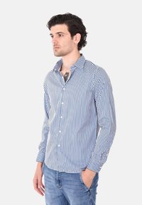Camicia a righe blu e bianca con maniche lunghe, colletto a punta e vestibilità rilassata. Realizzata in tessuto leggero.