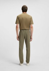 Khaki shirt met korte mouwen en olijfgroene broek met een relaxte pasvorm; de broek heeft een elastische tailleband en zijzakken. Witte sneakers.