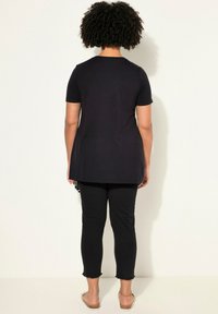 Tunic nera a maniche corte con scollo rotondo, abbinata a pantaloni neri a vita alta con orlo sfrangiato, indossata con sandali piatti.
