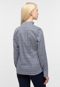 Camicia a righe blu navy e bianca con colletto, maniche lunghe e vestibilità slim. Presenta un design geometrico e una texture del tessuto liscia.